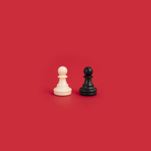 A white and a black pawn chess pieces on a bright red background - perfect for diversity and tolerance concepts