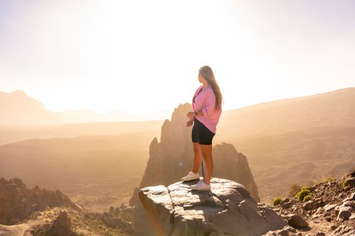 A young female tourist standing with a pink sweatshirt looking at the sunset in the natural area of Teide in Tenerife, Canary Islands, Spain