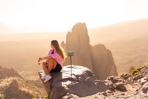 A young female tourist sitting with a pink sweatshirt looking at the sunset in the natural area of Teide in Tenerife, Canary Islands, Spain