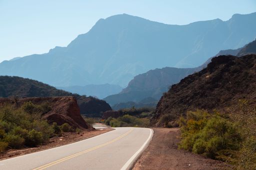 An open road surrounded with hills and green bushes on a sunny day