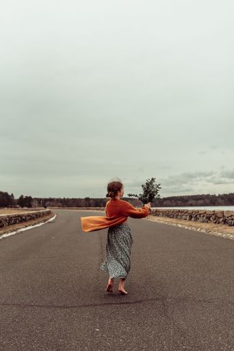 A vertical shot of a barefoot little girl holding a bouquet of flowers on an open road