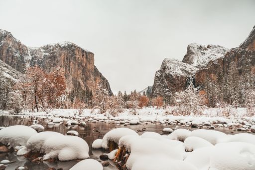 A beautiful view of a river, trees and mountains covered in snow during winter