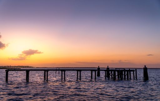 A beautiful view of a pier on the sea during sunset with cloudy sky