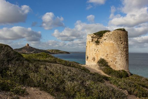 The old ruins and the sea in Sardegna, Italy against the cloudy blue sky