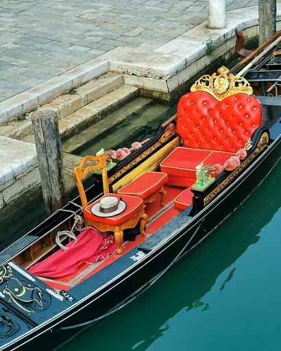 A vertical overhead shot of an old gondola with red luxury seats moored at a canal in Venice, Italy
