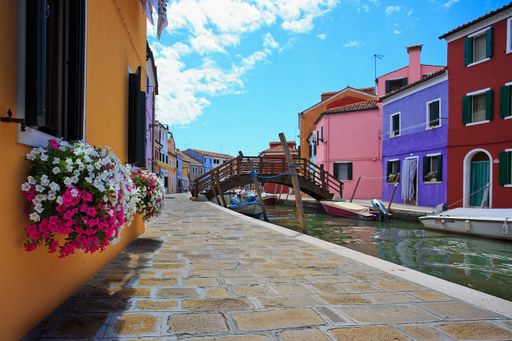 A scenic view of pavement against a wooden bridge on the water surrounded by colorful houses in Burano, Venice, Italy