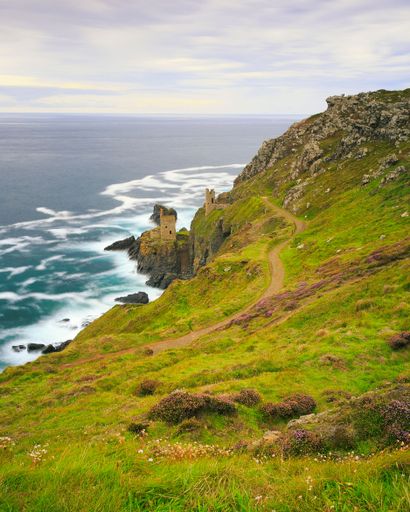 A vertical shot of a rocky coast covered with greenery against a seascape on a sunny day