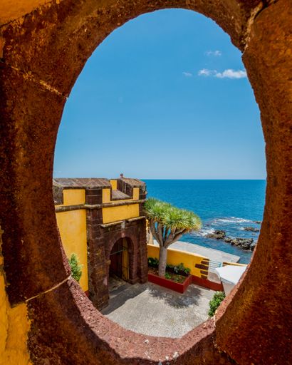 The Yellow castle of Sao Tiago with the blue sea from a big hole of old wall in Funchal, Madeira island