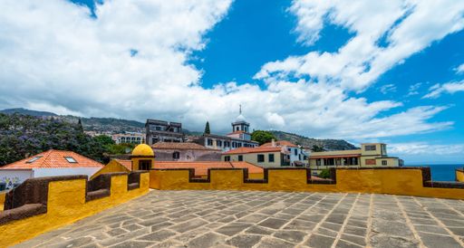 The buildings and mountain under cloudy sky from the roof of Yellow castle of Sao Tiago in Funchal, Madeira island