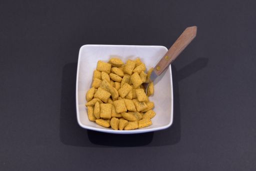 An overhead shot of crispy cereal pillow flakes in a white bowl isolated on a black background