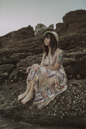 A selective focus shot of a young caucasian female with tattoos wearing a dress and straw hat
