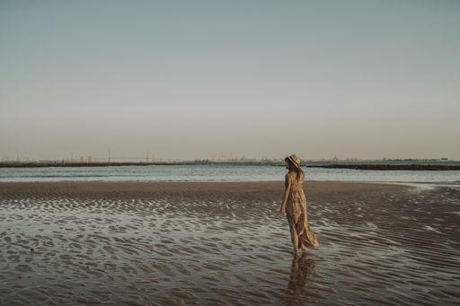 A young caucasian female wearing a dress and straw hat having fun on the seashore