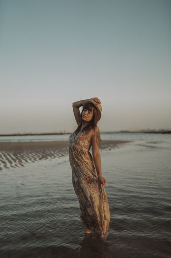 A young female with tattoos wearing a dress and straw hat on blurred ocean background