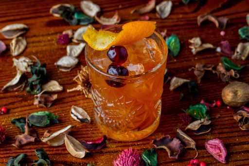 A closeup of a glass of Old fashioned cocktail on wooden table with dry flowers