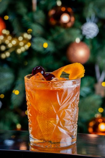 A vertical shot of a glass of Old fashioned cocktail with blur Christmas tree in the background