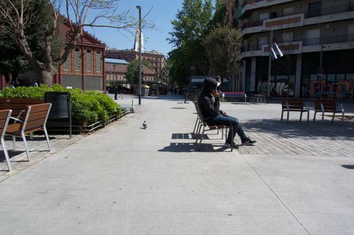 A side-view of a man in hoodie talking on the phone while sitting on street chair in Barcelona