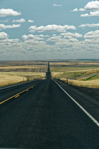 A vertical shot of long asphalt road through yellow fields on blue cloudy sky background