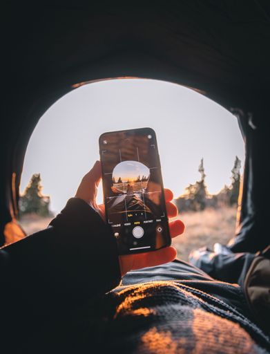 A Female hand taking photo of sunset by phone from tent