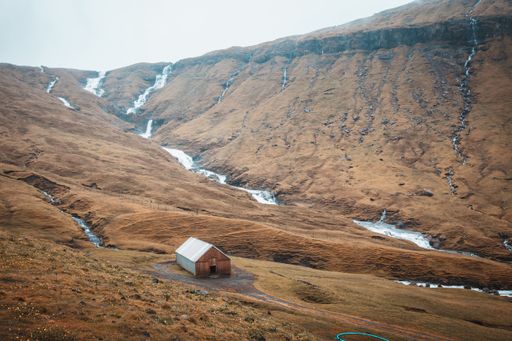 A beautiful scenery of a river surrounded by rocky cliffs under a cloudy sky in the Faroe Islands