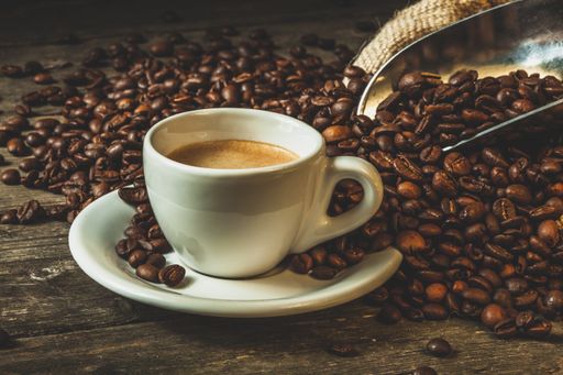 A closeup shot of a cup of coffee with spilled roasted coffee beans on the table