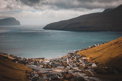 A high angle shot of buildings by the lake surrounded by rocky cliffs in the Faroe Islands