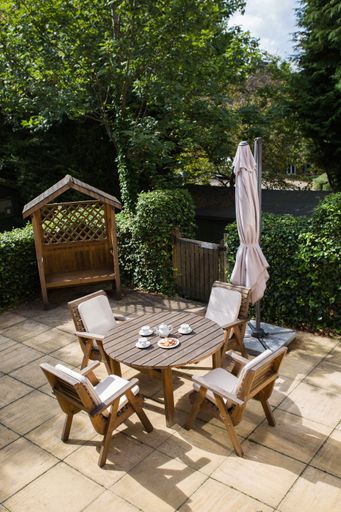 A vertical shot of a cozy corner in the park with wooden chairs and table for breakfast