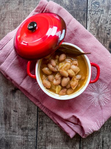 A high angle shot of cooked beans in a red bowl placed on a pink blanket