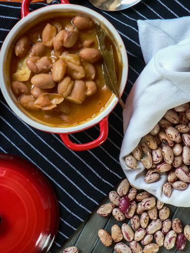 A shot of raw red beans in a white bag and cooked ones in a metal bowl with a striped texture under it
