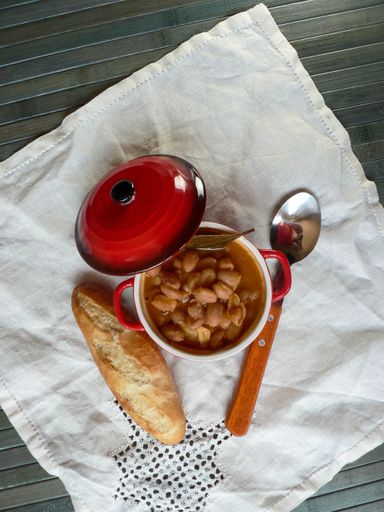An overhead shot of cooked beans, metal spoon, and bread on a white blanket