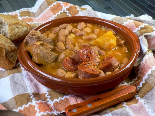 A high angle shot of bread and soup with beans and meat placed on the blanket
