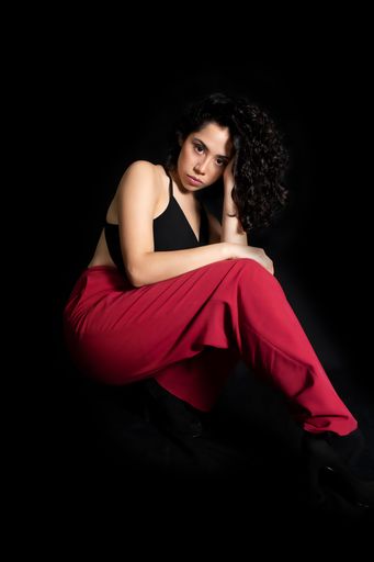 A beautiful Hispanic girl with curly hair modeling in front of the camera with a black back background
