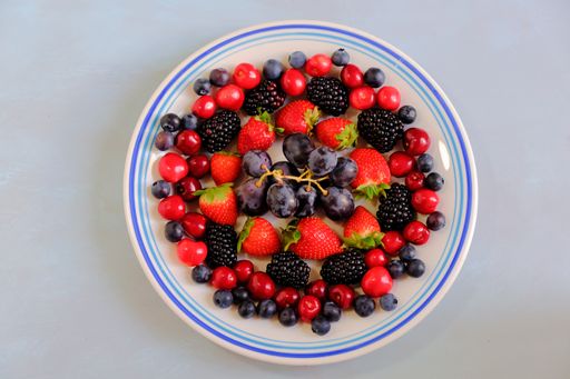 A high angle shot of a plate of grapes, strawberries, cherries, blackberries, and blueberries