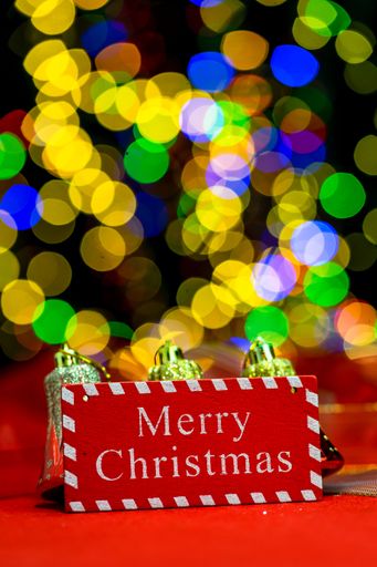 A vertical shot of a Merry Christmas signboard against colorful  bokeh lights