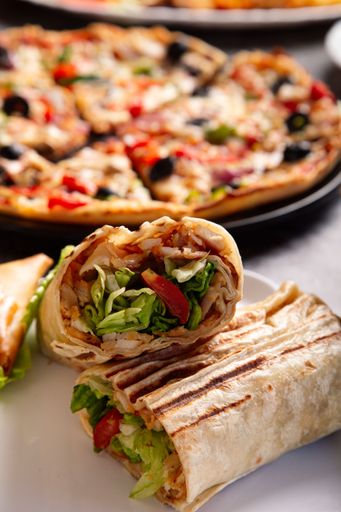 A selective focus shot of chicken shawarma with sliced pizza in the background
