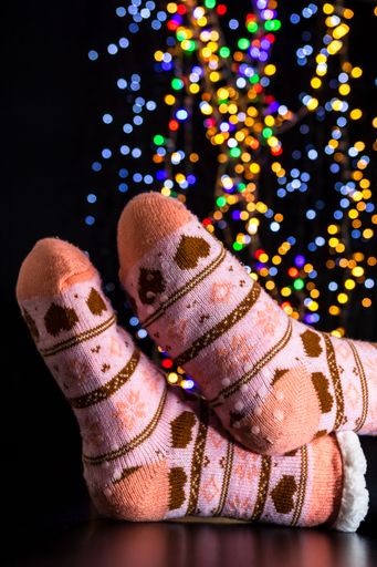 A vertical shot of someone wearing Christmas-themed socks in the background of bokeh lights.