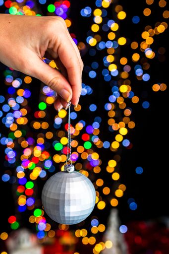 A vertical shot of a hand holding a Christmas white ball decoration with bokeh Christmas lights