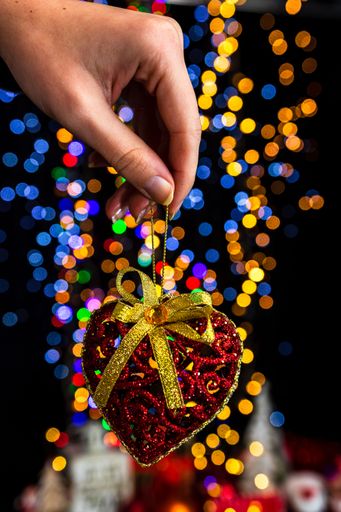 A vertical shot of a red glittery heart ornament against bokeh Christmas lights background