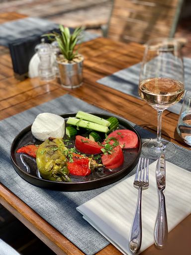 The fresh vegetables served in a black plate, with a fork, a knife and a glass of rose wine