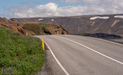 A long asphalt road surrounded by high mountains under the cloudy sky
