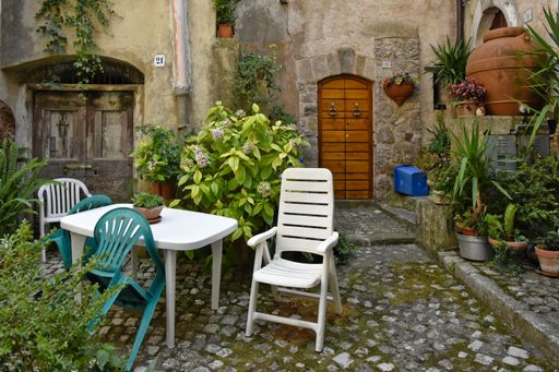 The empty chairs around the table on the street surrounded by green vegetation. Lenola, Lazio, Italy.