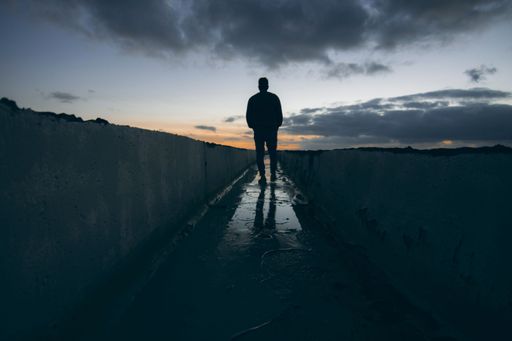 A silhouette back shot of a man walking in a wet narrow path