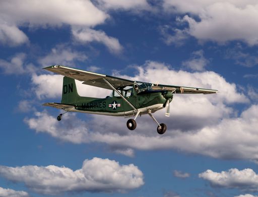 An army green propeller airplane flying in a cloudy sky