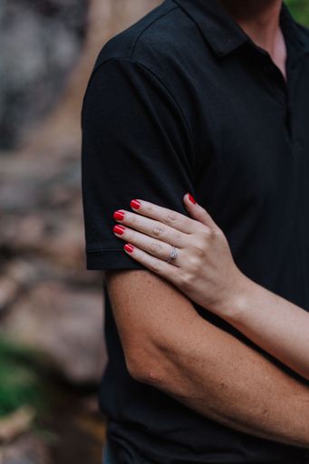 A beautiful portrait of a female hand showing her engagement ring while putting her hand on her fiance arm outdoors with blurred background