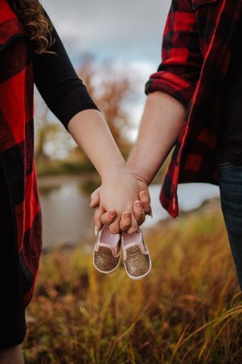 A closeup shot of a couple walking hand in hand and holding a baby boot in daylight in a green field