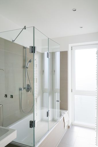 A vertical shot of a modern white bathroom with shower that has glass doors