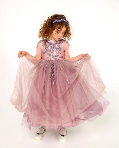 Beautiful little girl with curly hair in pink festive dress poses in front of camera on white background