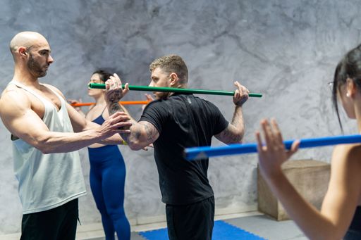 Fitness trainer helping group of people doing exercises with bar in the gym. Workout concept, copy space