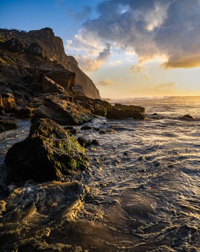 A beautiful shot of coastlines with large rocks under cloudy sky at sunset