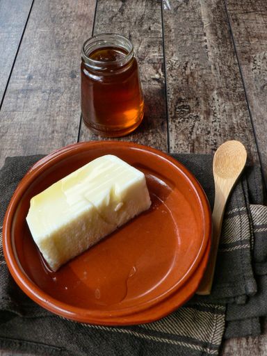 A vertical shot of a stick of butter in an orange plate, next to a jar of honey and a wooden spoon