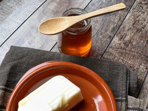 A closeup shot of fresh curd in a bowl with honey in a glass container and a wooden spoon on a table